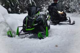 Two bundled-up people driving snowmobiles